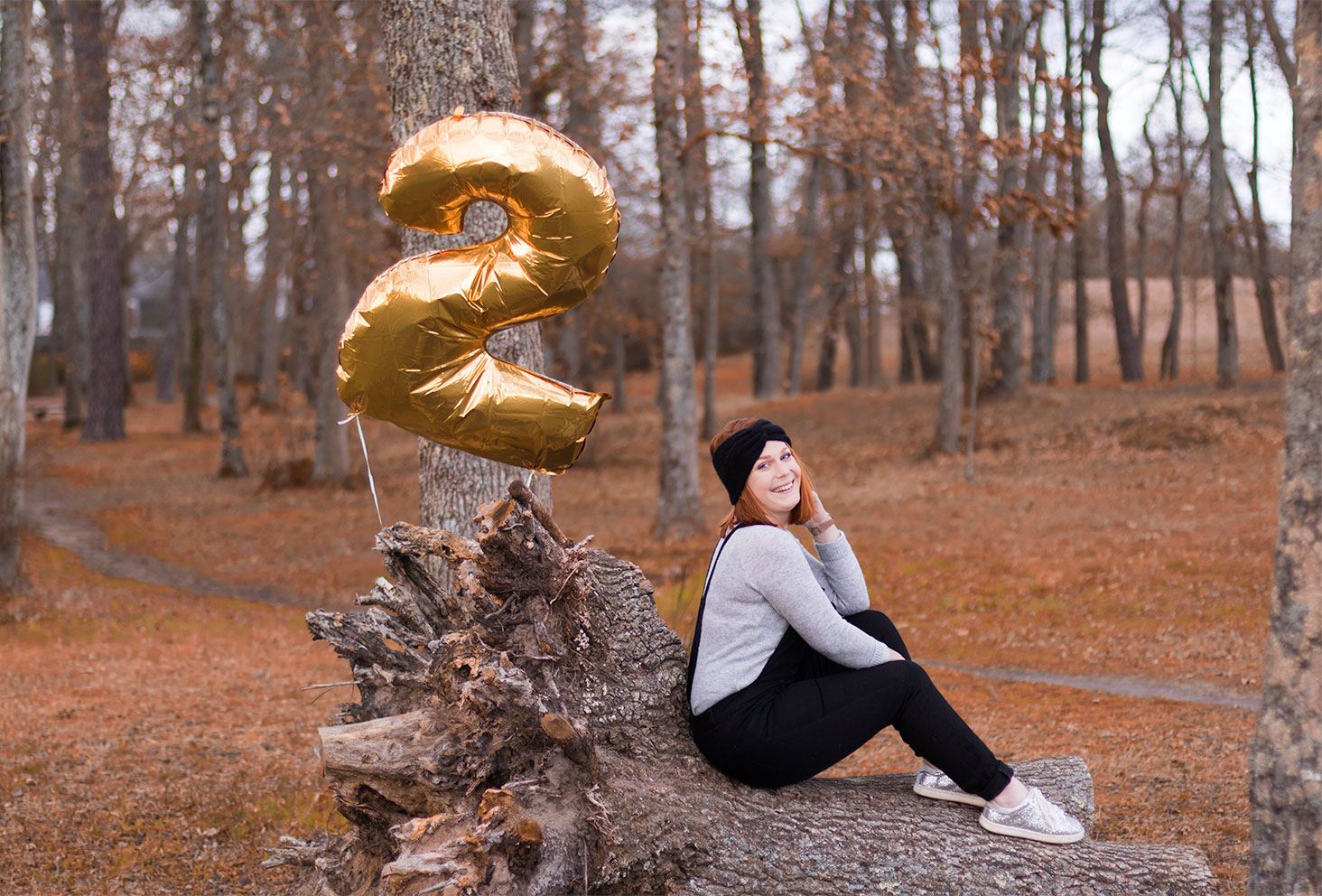Assise sur une souche d'arbre dans la forêt avec un ballon en forme de 2 pour les 2 ans du blog
