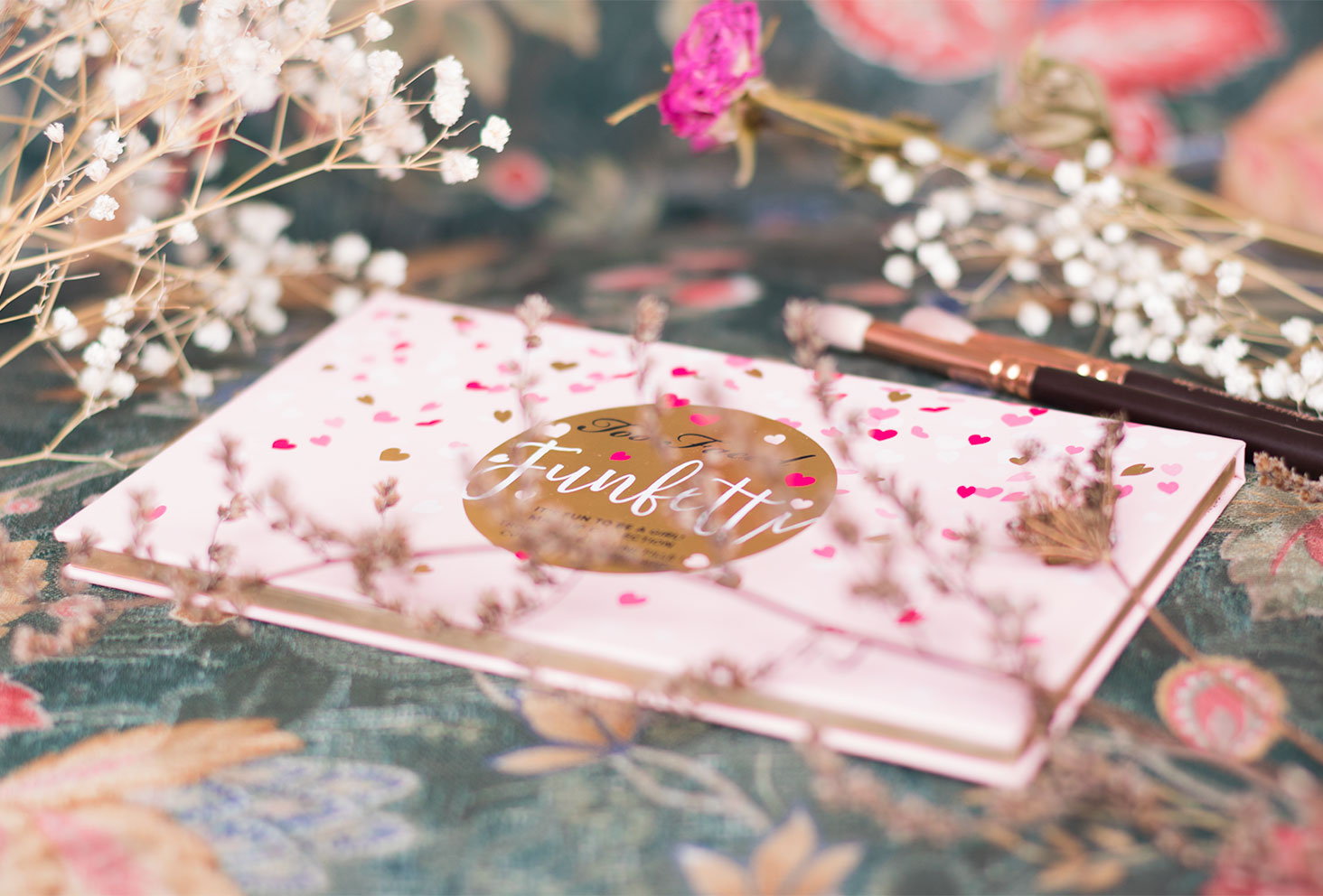 la palette Funfetti de Too Faced avec des pinceaux Zoeva cachés derrière les fleurs séchées