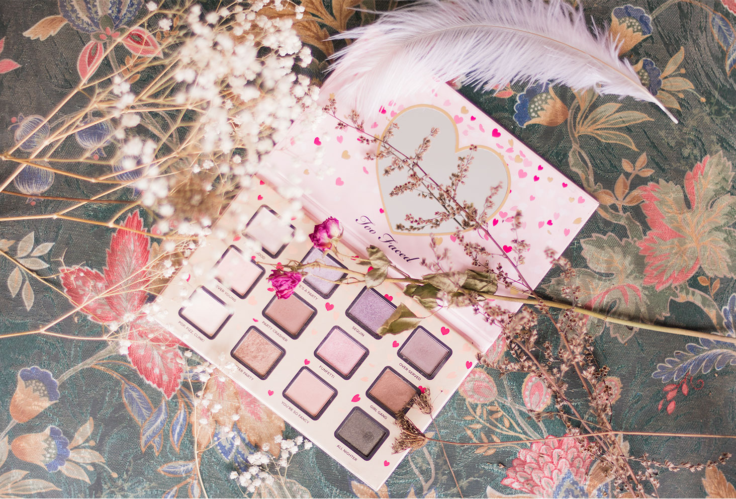 La palette Funfetti de Too Faced ouverte, posé sur un fauteuil fleuri entouré de fleurs séchées