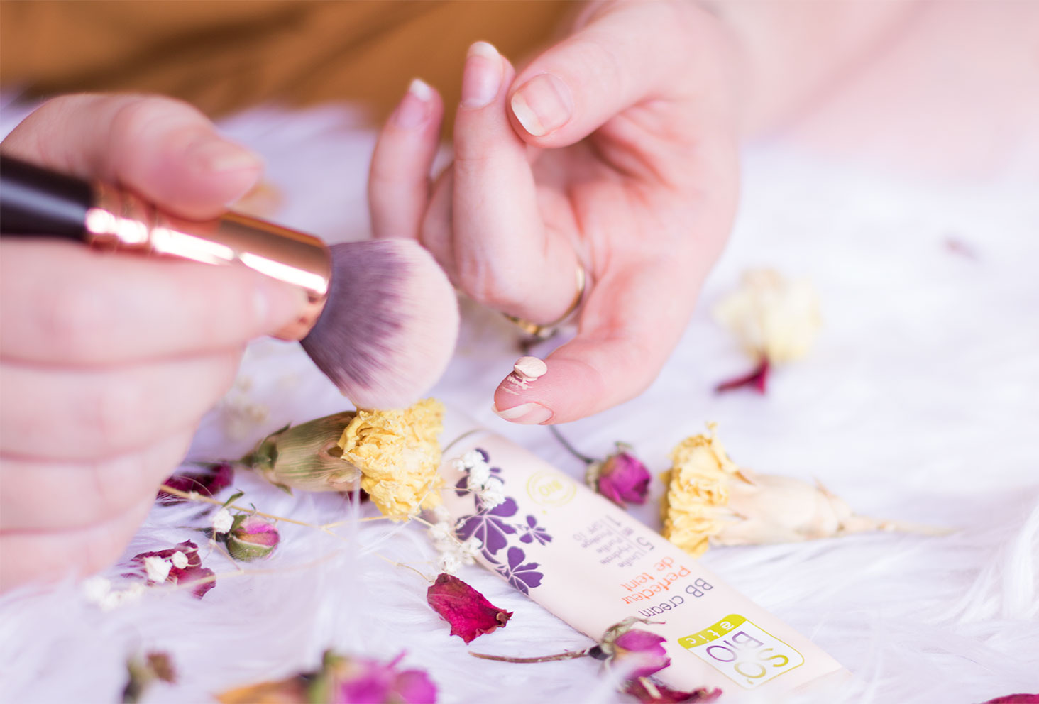 Zoom sur la texture de la BB crème de SO'BiO étic sur le bout du doigt avec le pinceau et les fleurs séchées à côté