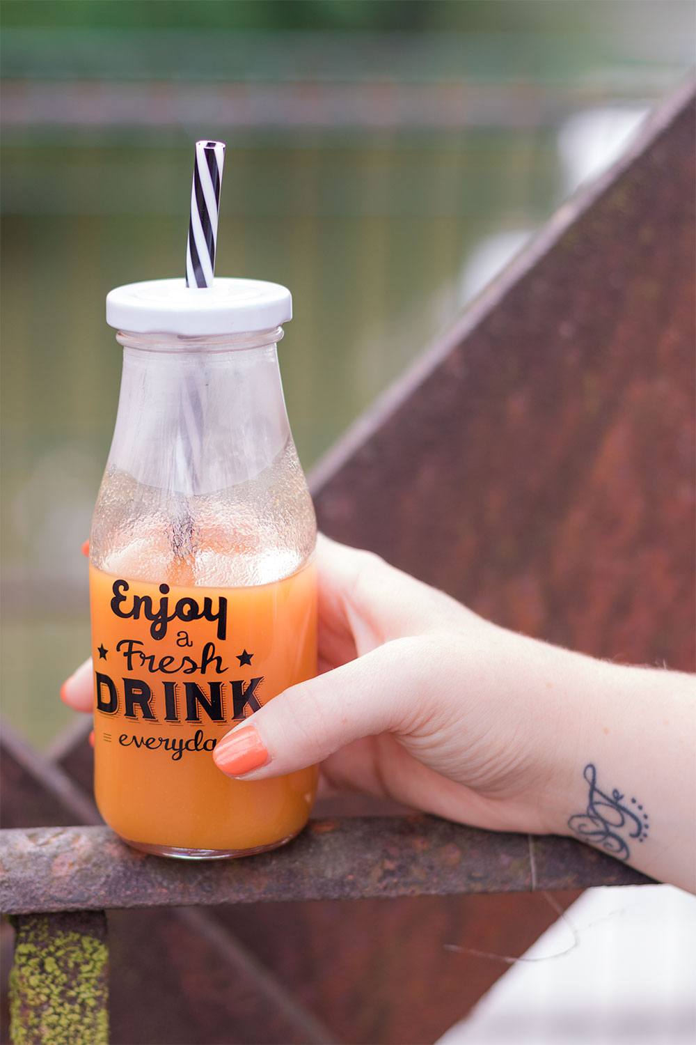Zoom sur le nectar d'abricot dans une bouteille en verre avec pour inscriptions "Enjoy a fresh drink everyday", posé sur une rambarde en métal