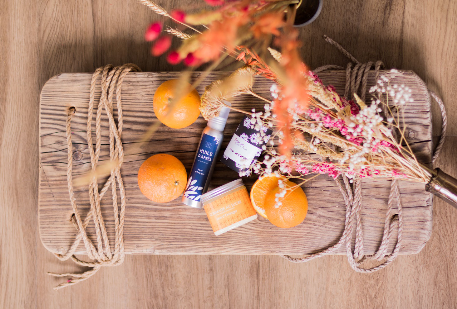 Le gommage, l'huile et le savon Sento de L'art du Bain, vu de haut, sur une planche en bois au milieu des oranges et des fleurs séchées