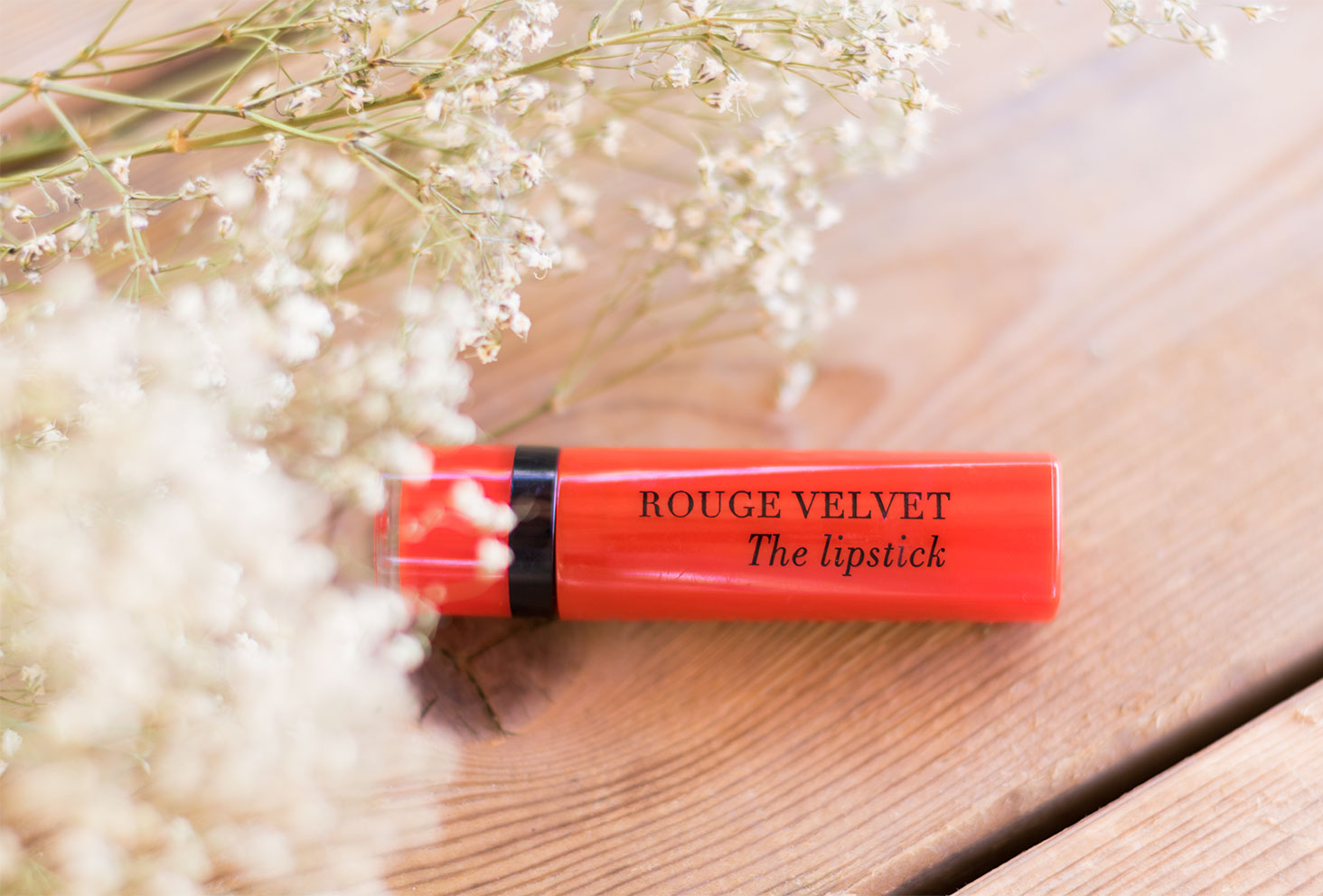 Rouge à lèvres rouge Velvet The Lipstick de Bourjois, sur une table en bois au milieu des fleurs séchées blanches