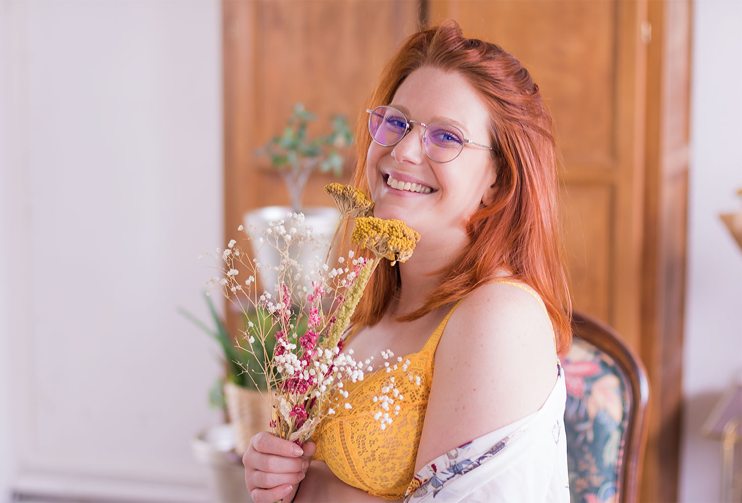 Zoom sur le soutien-gorge jaune en dentelle Pomm'Poire, de profil avec un bouquet de fleurs sèches entre les mains avec le sourire