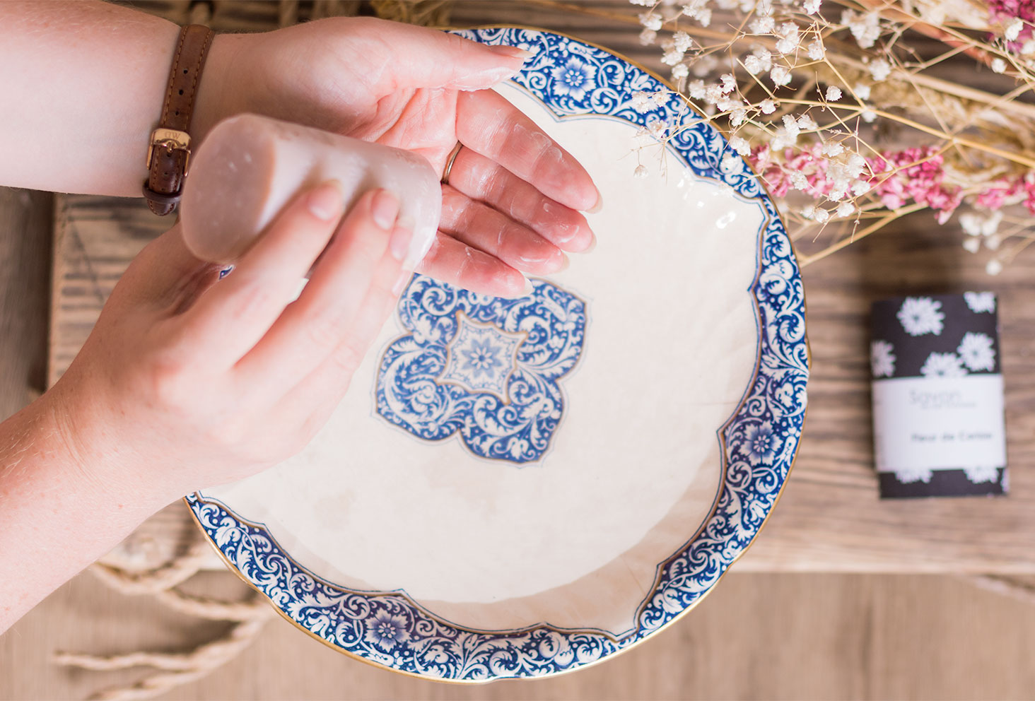 Utilisation du savon Sento au lait d'ânesse de L'art du Bain au dessus des fleurs séchées dans une vasque en porcelaine bleue et blanche