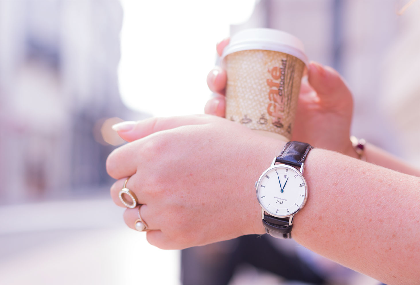 La montre marron Dapper Work de Daniel Wellington portée avec un café à emporter dans la main