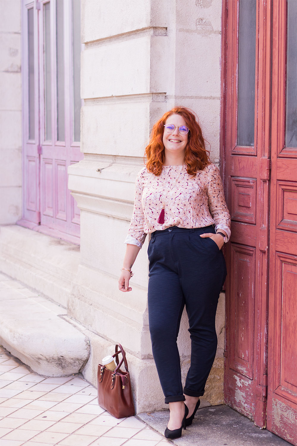 Le dos contre le mur en pierre blanc du grand théâtre de Tours, en blouse rose La Morue entrée dans le pantalon bleu marine Kiabi et escarpins noirs en velours