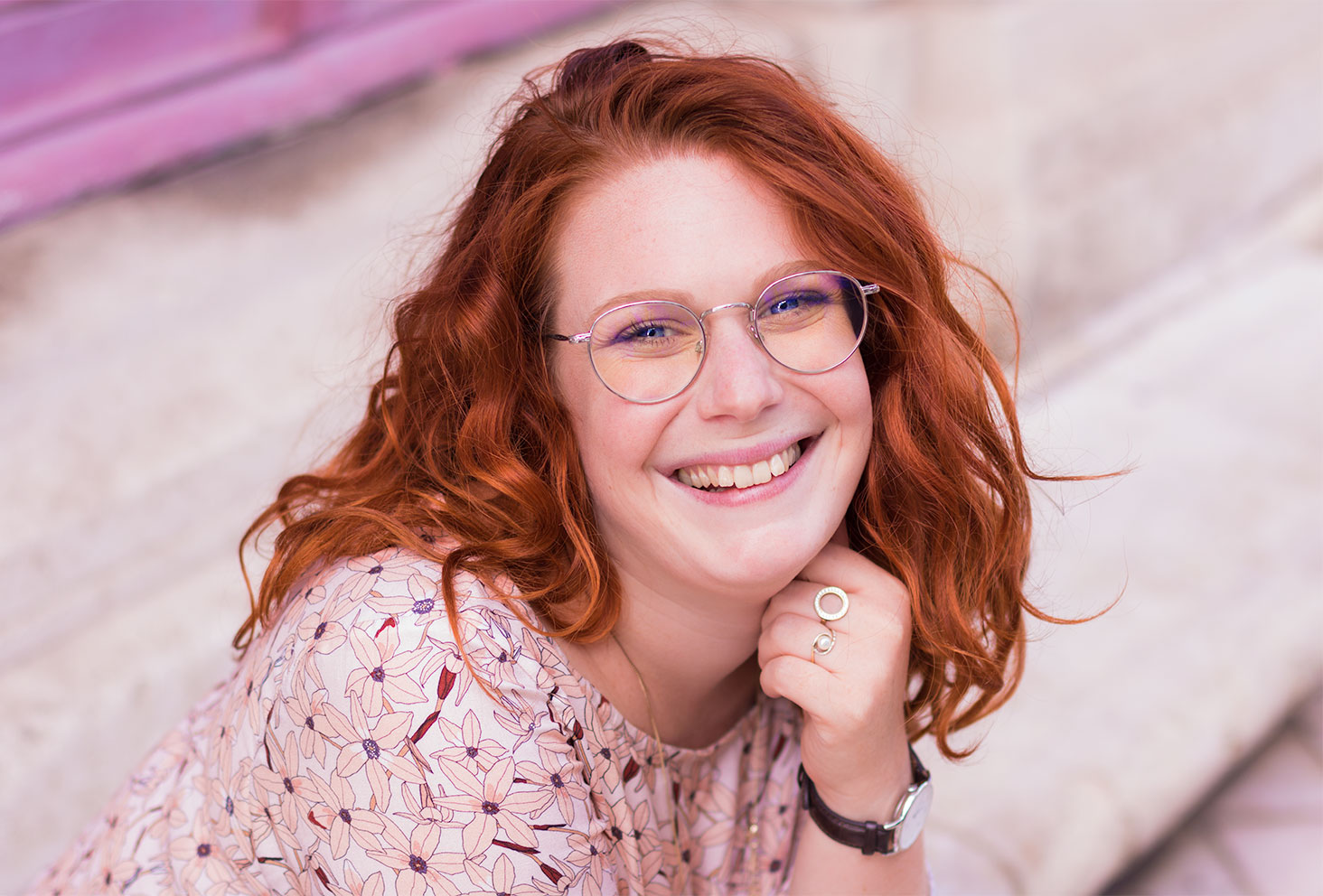 Portrait de profil, cheveux roux bouclés et lunettes style aviateur argenté devant les yeux bleus. Le visage appuyé sur le poing avec la montre marron Daniel Wellington