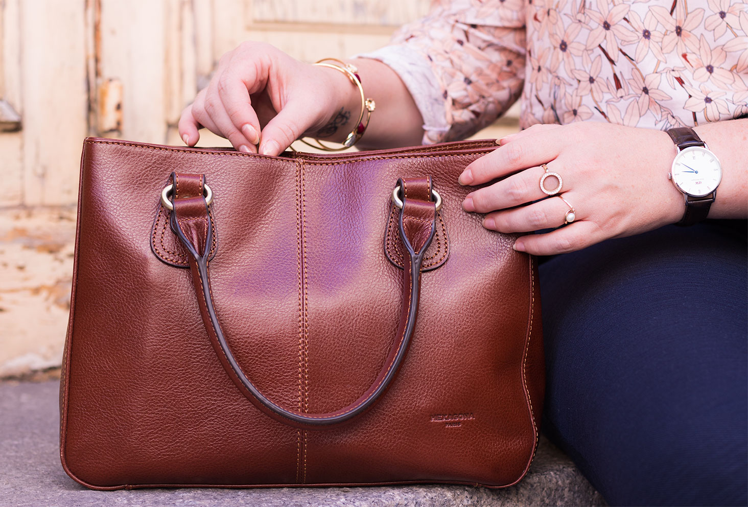 Zoom sur le sac marron en cuir Hexagona Paris posé sur des marches en pierre, les mains entrain d'ouvrir la fermeture