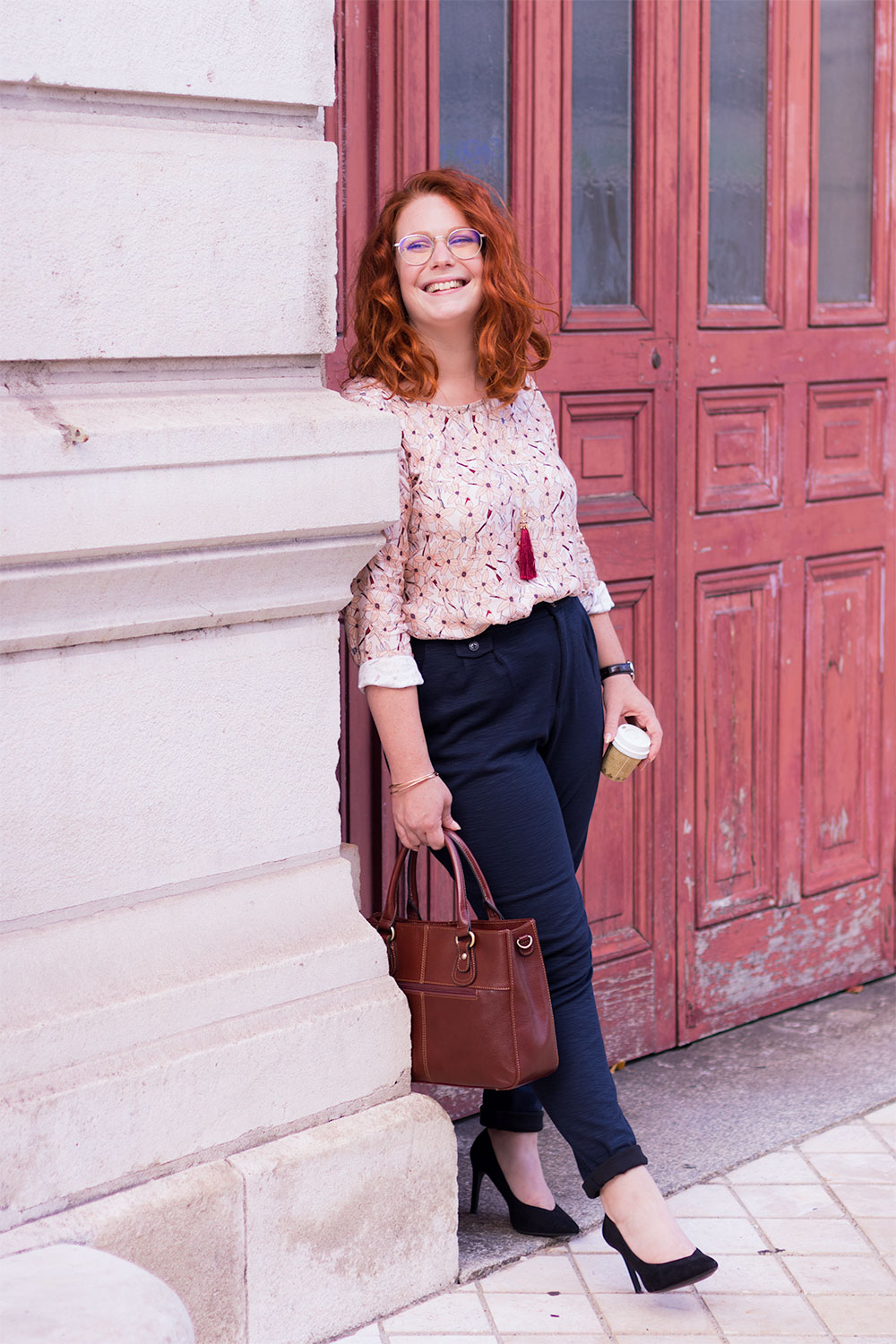 Appuyé contre le mur en pierre, davant une grande porte en bois orangée du grand théâtre de Tours, avec des escarpins à talons hauts noirs pour un look de working girl