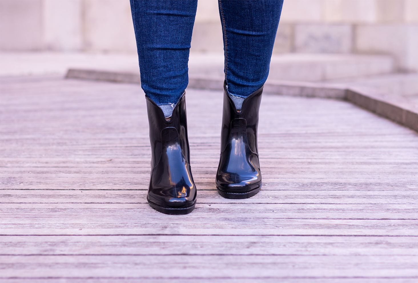 Les bottines en plastique noires de La Halle portées de face avec un jeans sur une passerelle en bois