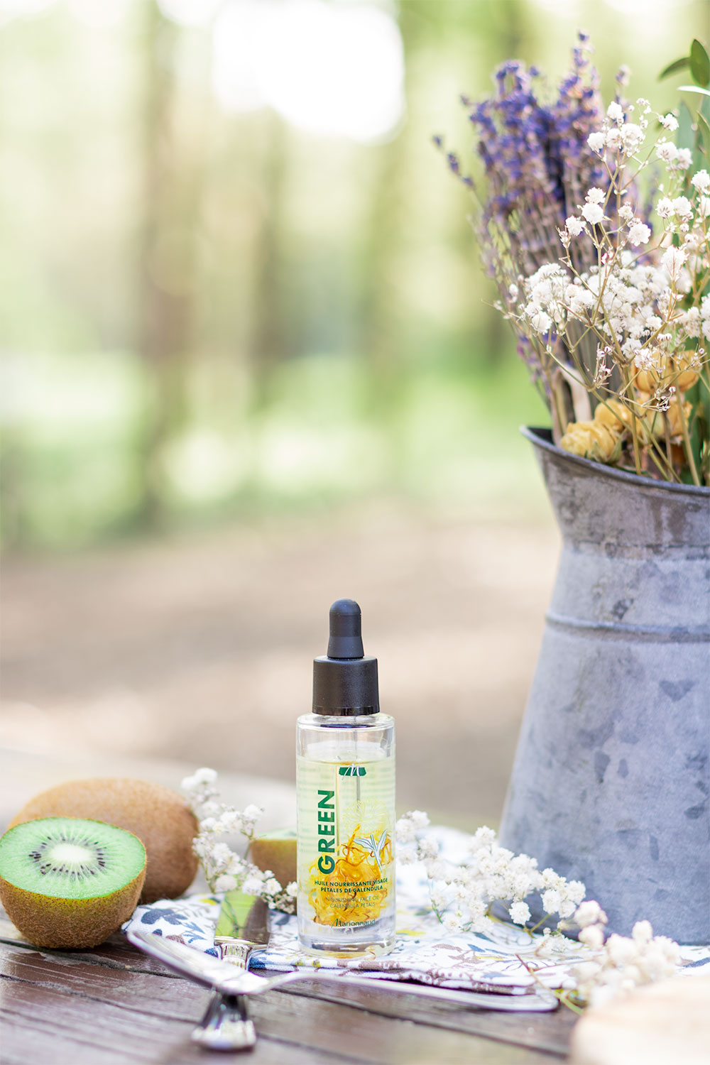 L'huile nourrissante visage de la gamme Green de Marionnaud posé sur une table en bois entourée de kiwis et de fleurs séchées