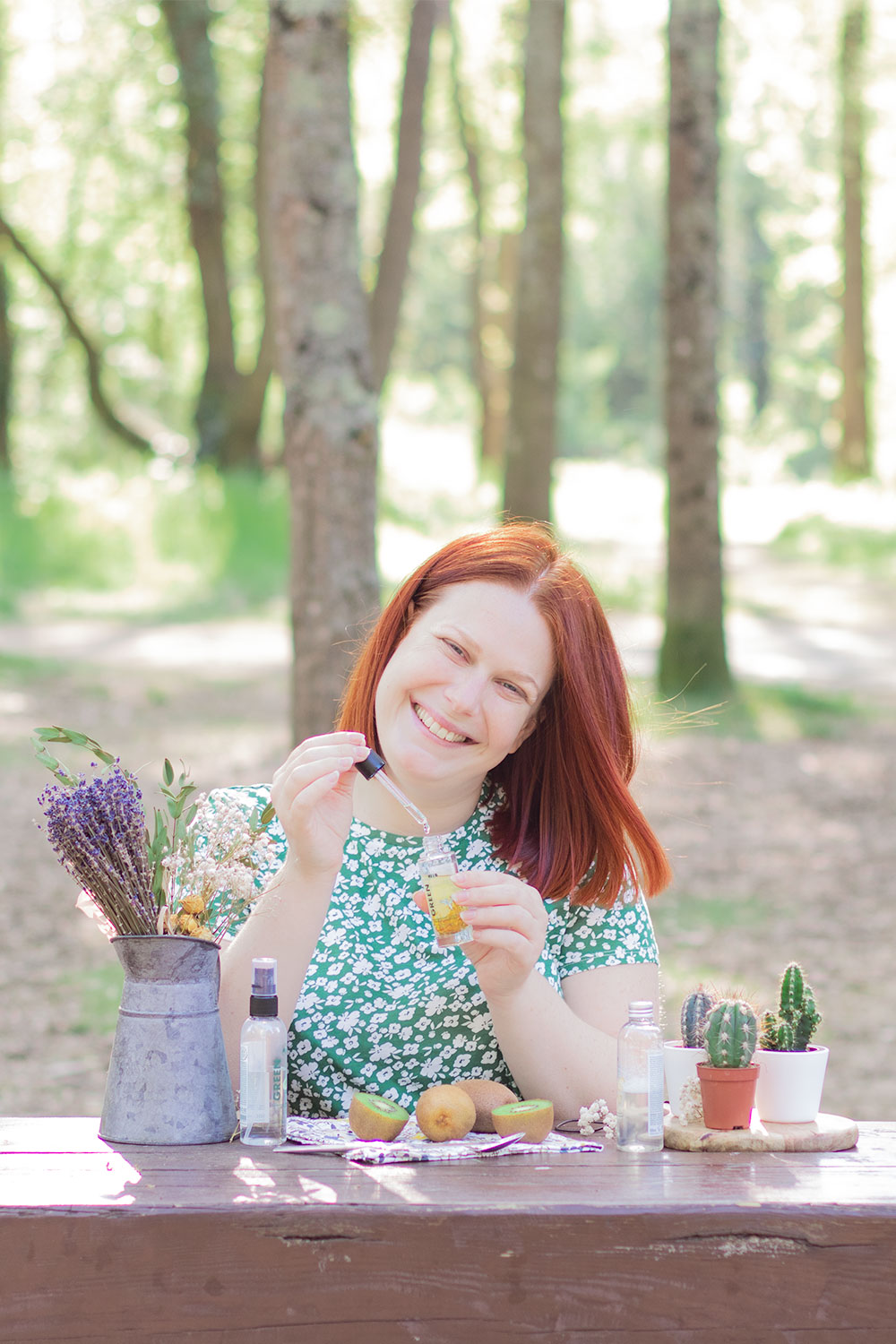 Utilisation de l'huile nourrissante visage de Marionnaud sur une table en bois au milieu des bois, en t-shirt vert fleuri avec le sourire