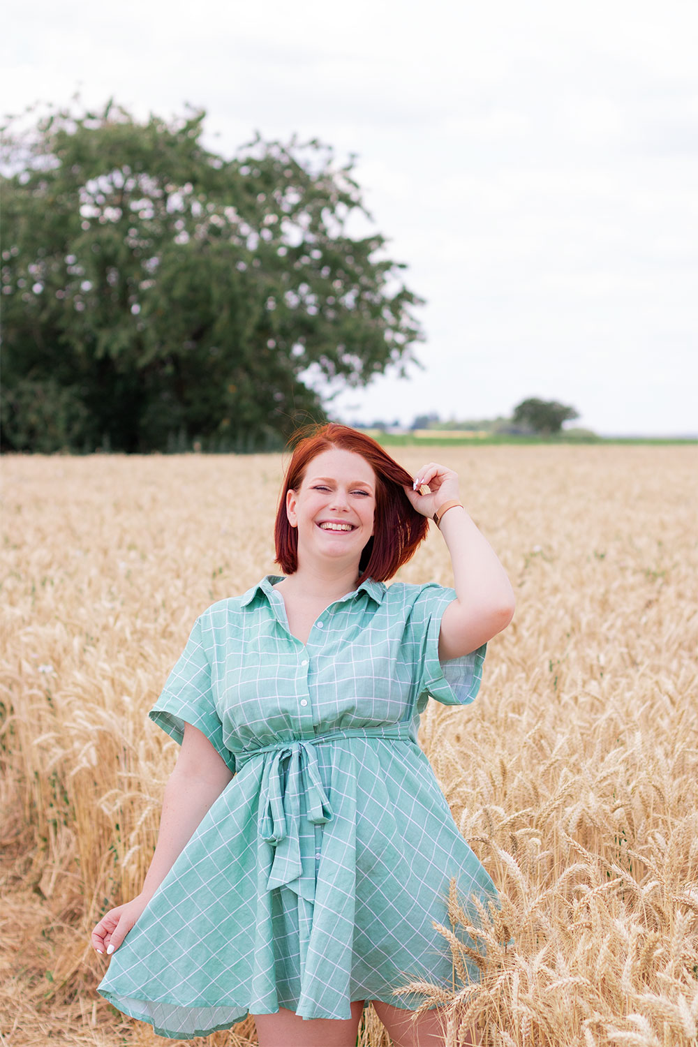 Robe chemise verte et fluide Shein portée avec une main dans les cheveux et le sourire au milieu d'un champs de blé