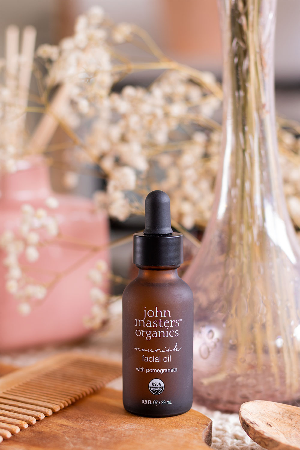 Zoom sur le packaging en verre marron et noir typique de John Masters Organics de l'huile hydratante pour le visage, sur une planche en bois