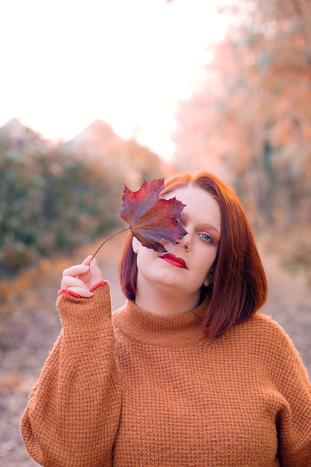 Make-up coloré au couleurs de l'automne, au milieu de la forêt, une feuille bordeaux devant l'oeil droit