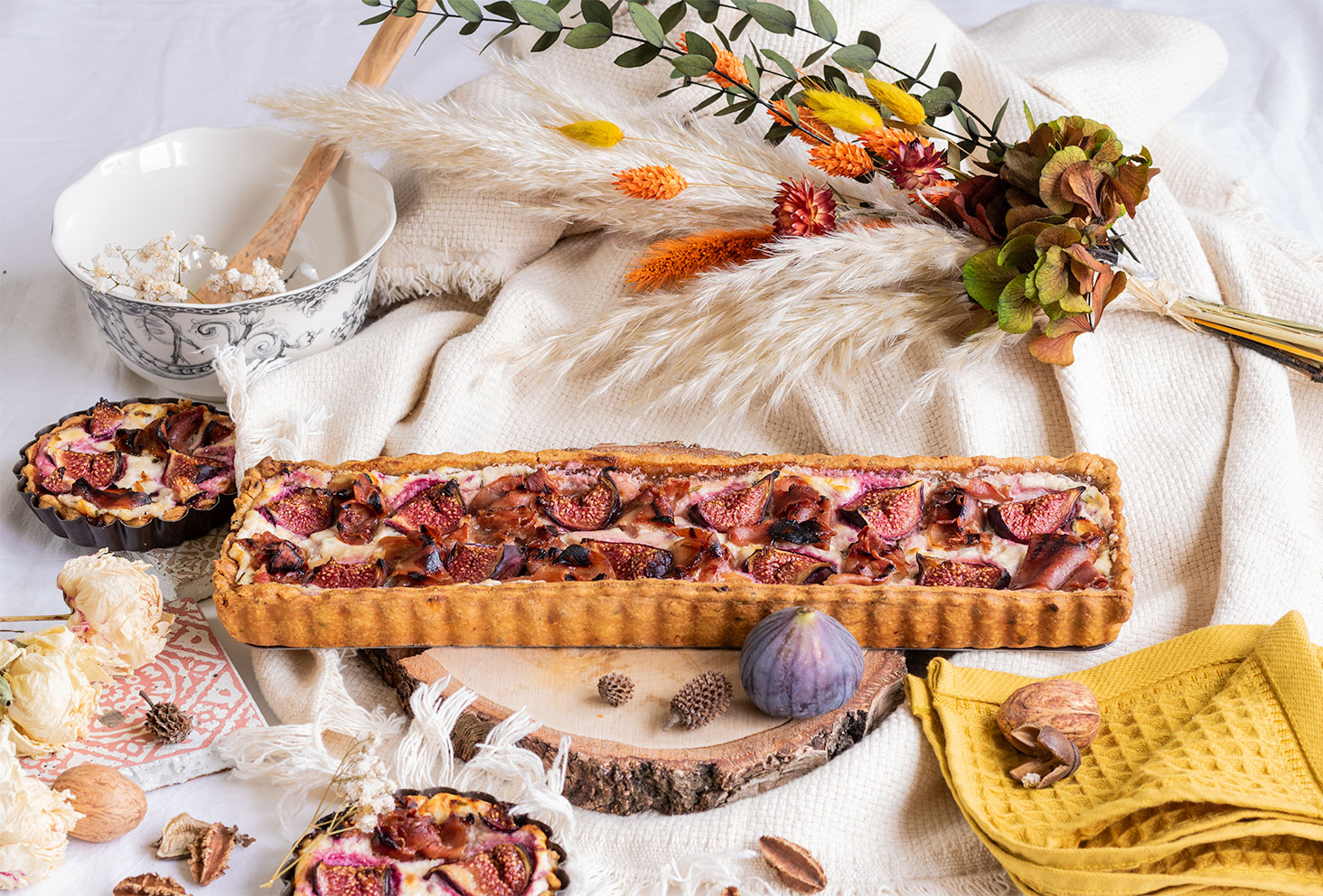 La recette de la tarte sucrée salée aux figues et au jambon, posée sur une planche en bois au milieu d'un décor d'automne