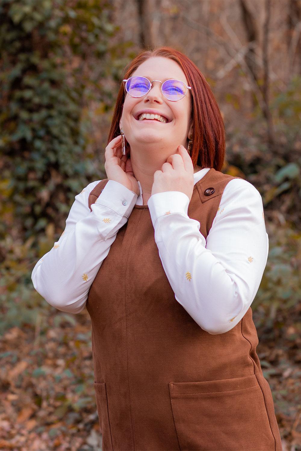 La blouse en Tencel de la marque Mardi Matin sous une robe chasuble marron, portée au milieu des bois avec le sourire aux lèvres