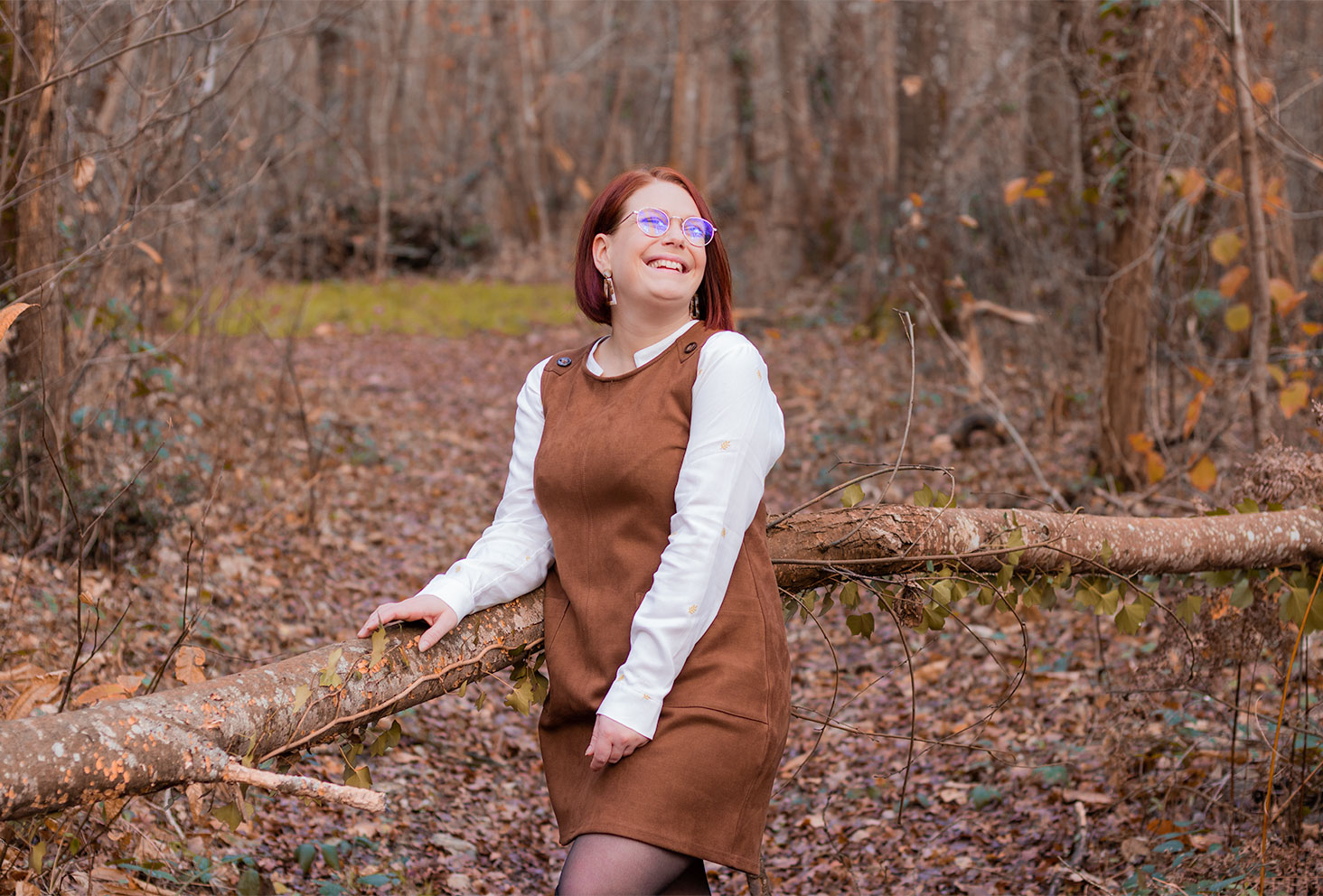 Accoudée à un arbre tombé au milieu des bois, avec le sourire en robe chasuble marron