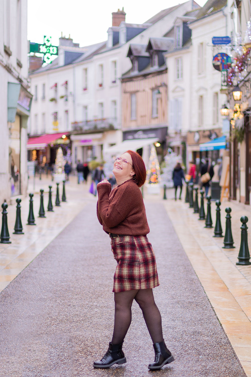 Au milieu d'une rue au plein cœur de la ville d'Amboise, de profil avec le sourire, en pull et jupe en laine marron