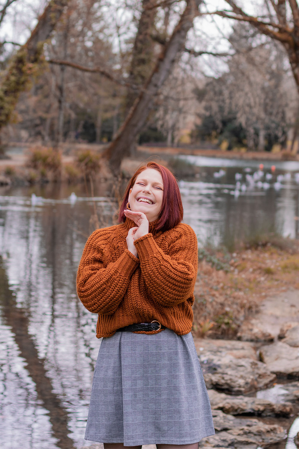 Au bord d'un lac en robe à carreaux et pull marron oversize, ceinturé à la taille, avec le sourire