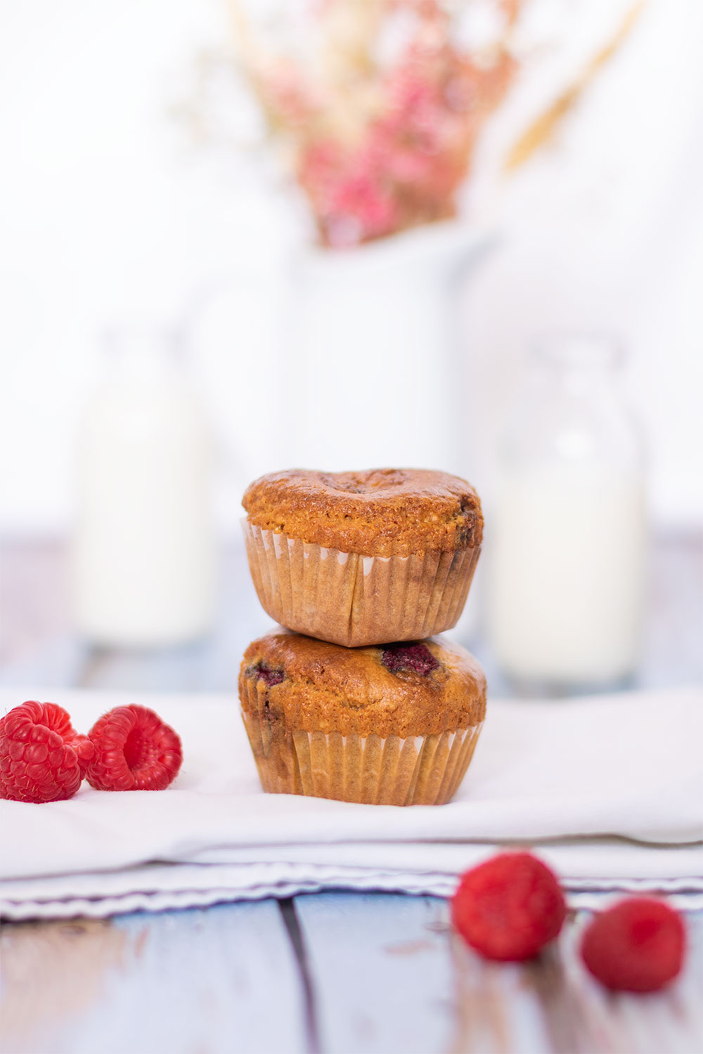 Zoom sur deux muffins aux framboises posé l'un sur l'autre au milieu de framboises sur un torchon blanc