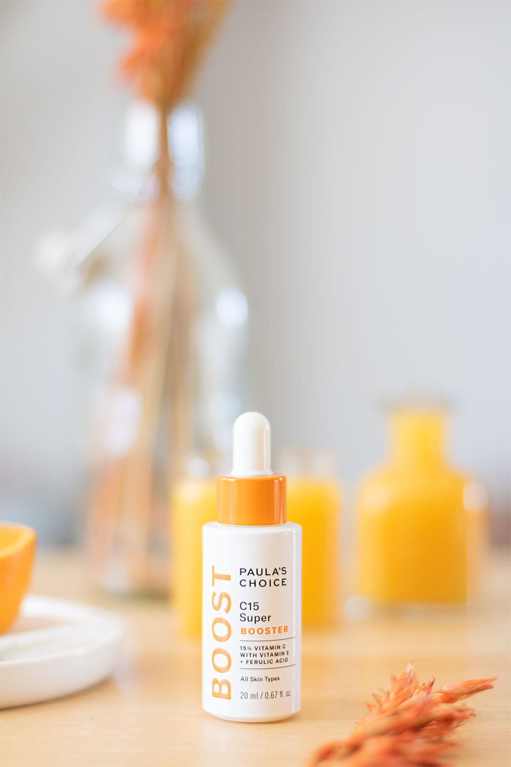 Le sérum concentré en vitamine C de Paula's Choice sur une table en bois devant des bouteilles de jus d'orange