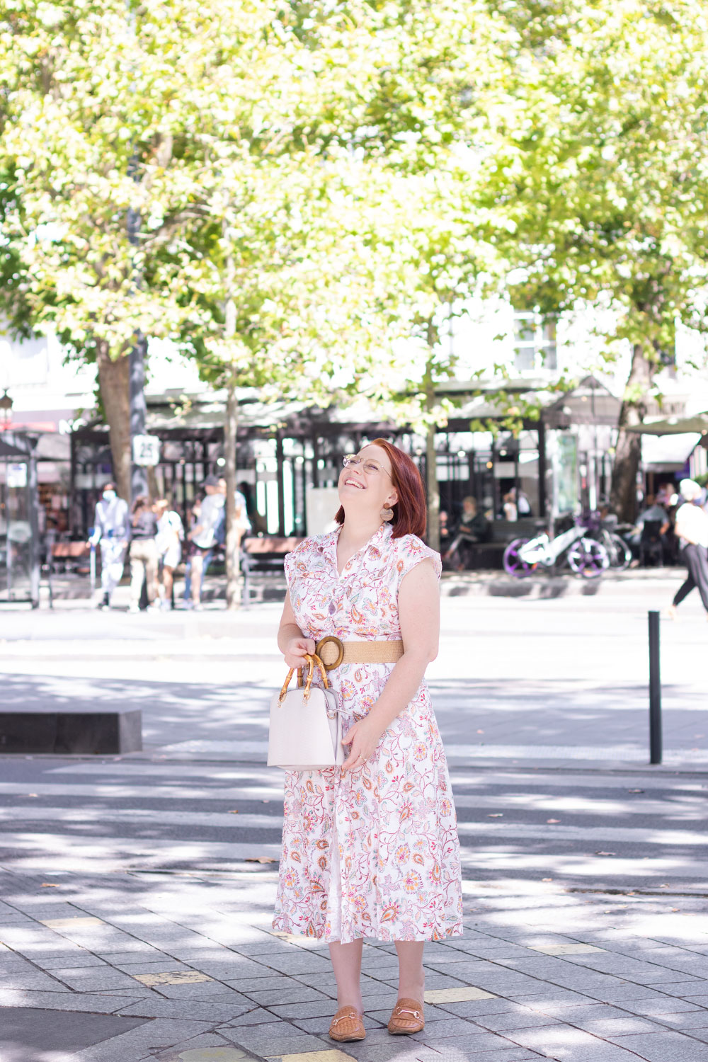 Dans la rue, le sac à main beige dans les mains, en robe chemise à fleurs