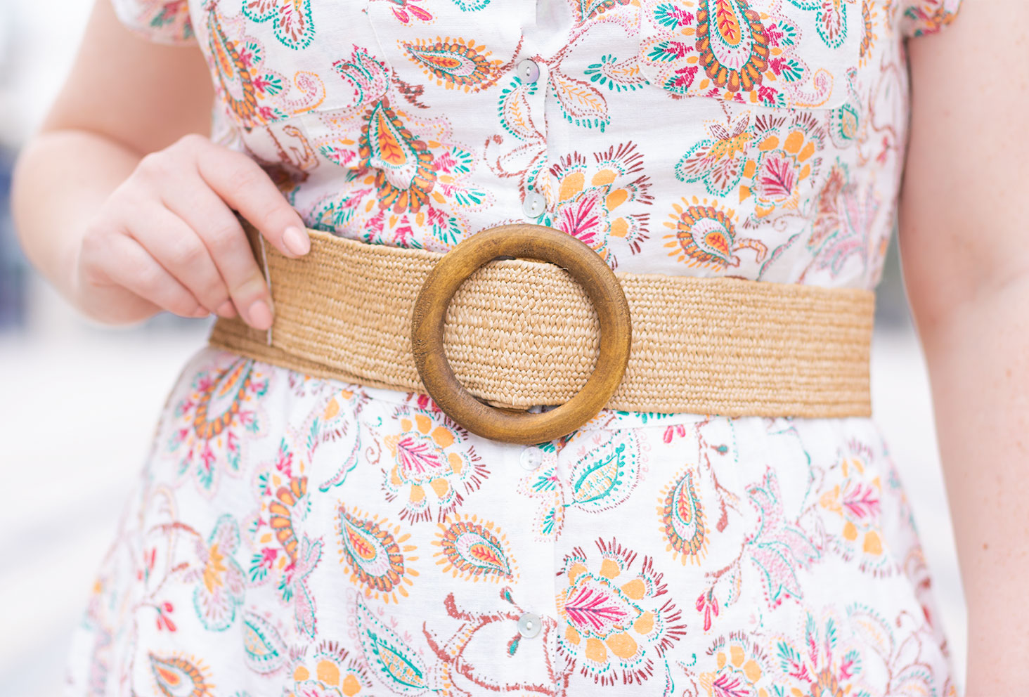 Zoom sur une ceinture épaisse en paille avec fermoir en bois, portée sur une robe chemise en lin aux motifs fleuris