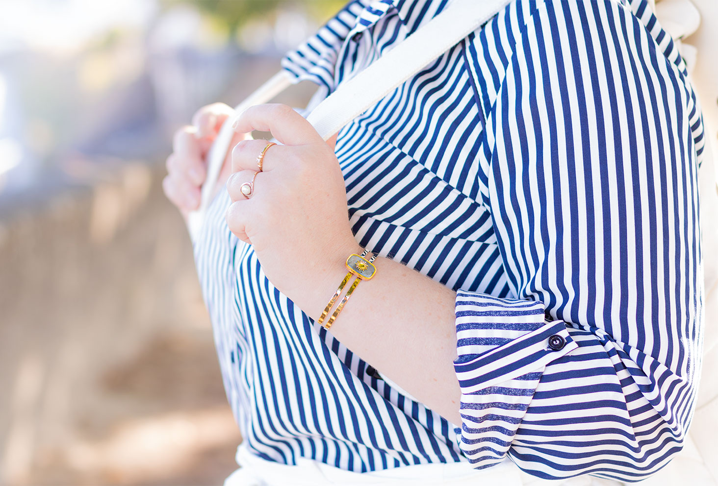 Zoom sur un jonc doré porté avec une chemise à rayures bleues et blanches