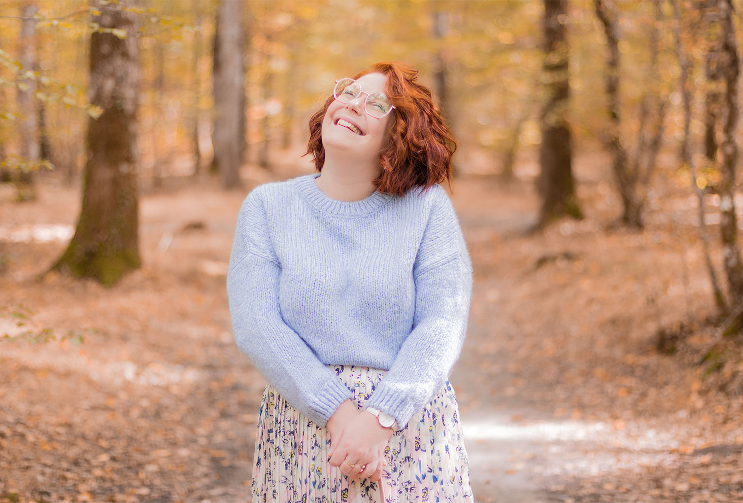 Zoom sur le pull court en laine bleu pastel porté avec le sourire au milieu des bois d'automne