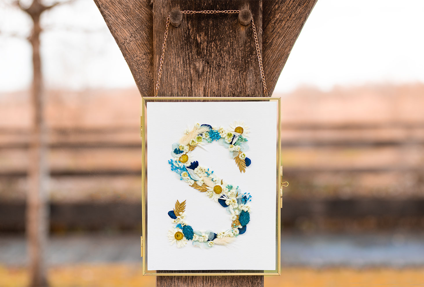 Une lettre en fleurs séchées dans un cadre doré accroché à une poutre en bois