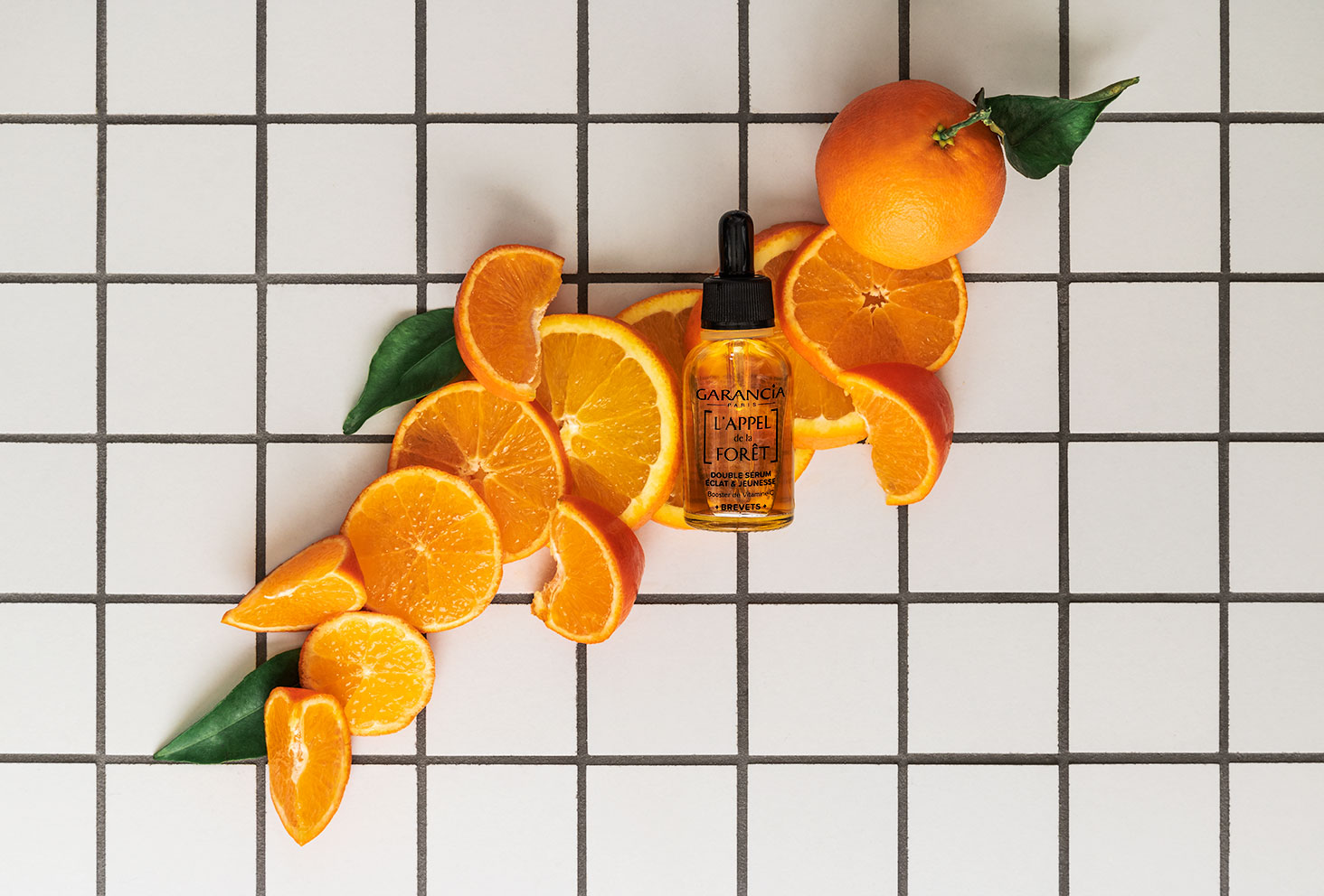 Clémentines et oranges sur un carrelage blanc pour mettre en avant le sérum orange à la vitamine C de Garancia