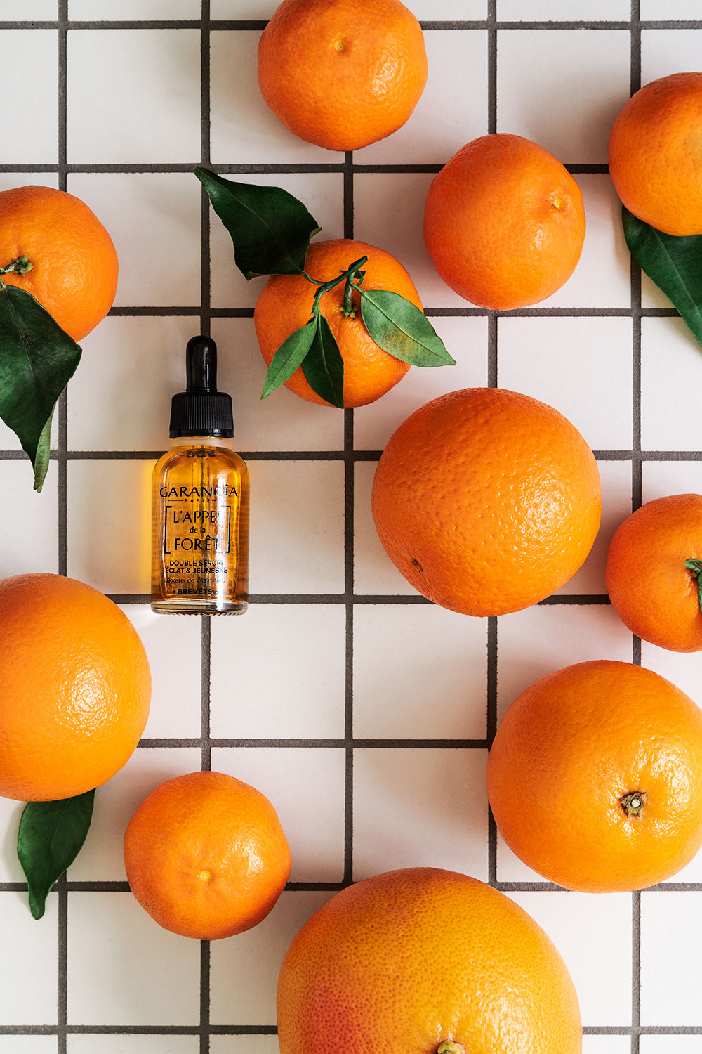 Le sérum à la vitamine C de Garancia posé sur du carrelage au milieu d'oranges et de clémentines entières