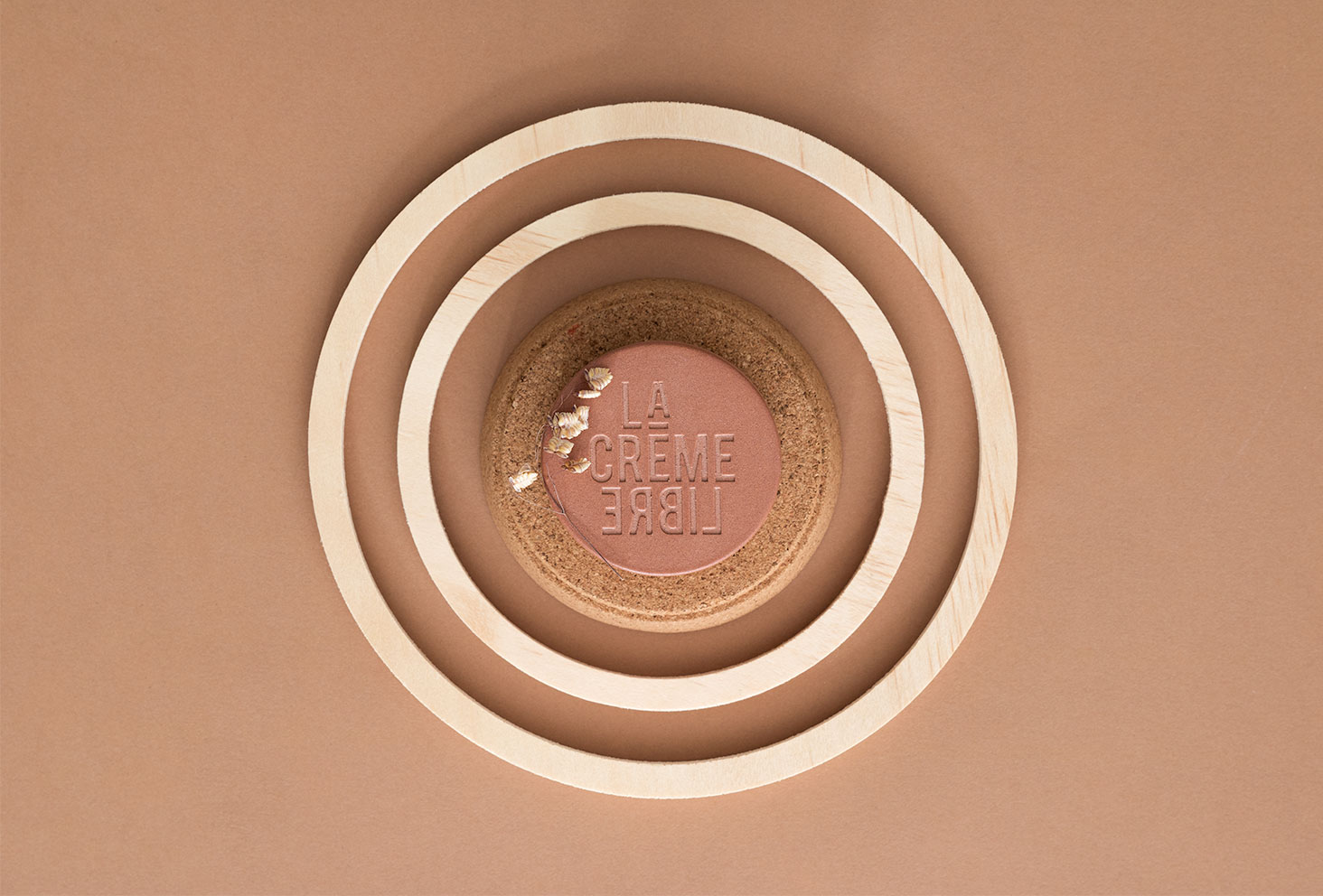 Zoom sur la crème riche de La Crème Libre dans un pot en béton couleur terracotta posé sur un fond marron au milieu de cercles en bois clairs