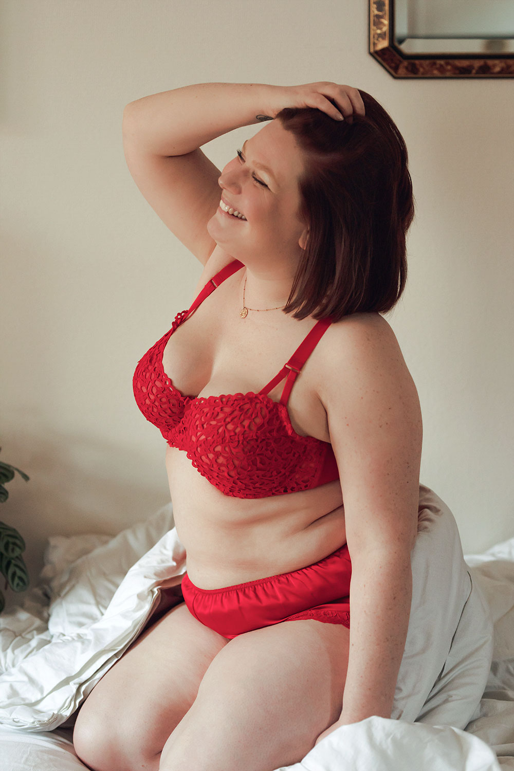 Zoom sur l'ensemble de lingerie rouge de la marque Valège porté, assise sur un lit avec le sourire et une main dans les cheveux