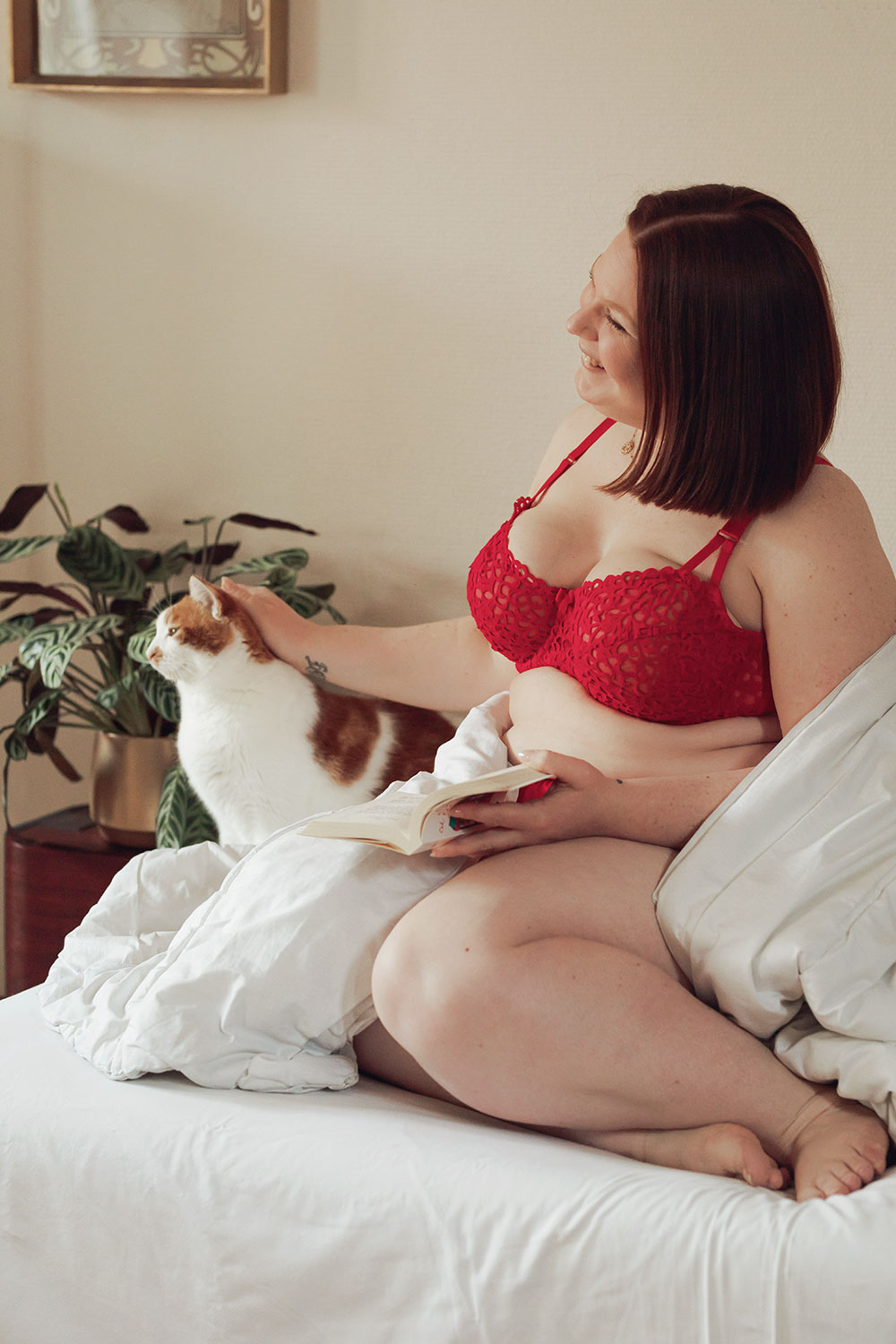 Assise sur mon lit avec le chat, en lingerie rouge , sous la couette avec le sourire