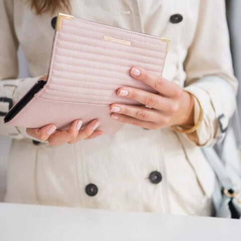 Portefeuille rose tenu entre les mains avec un trench beige